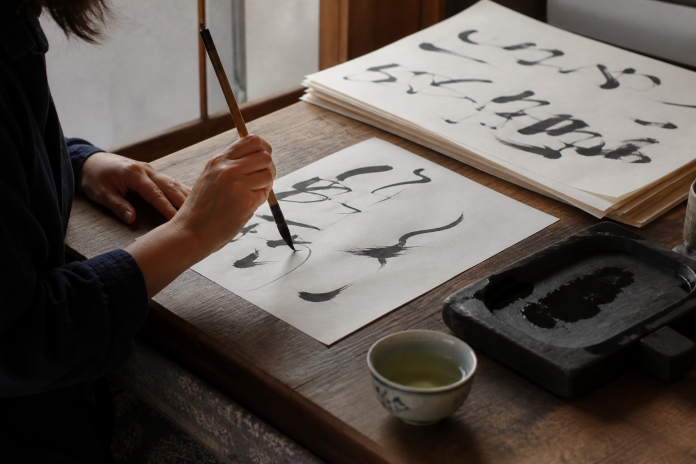 Brush practice at a low table Close-up of a person practising calligraphy with a brush on paper at a low table, ink stone and a cup of tea beside them