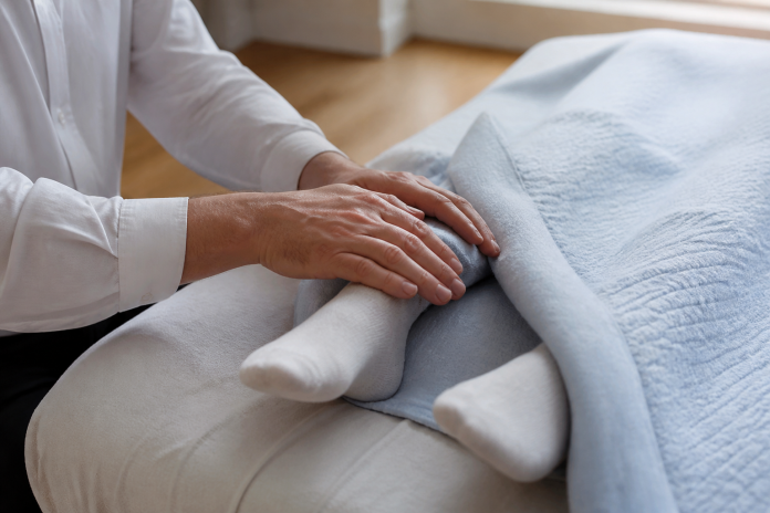 Hands resting at the feet Close-up of a practitioner's hands resting lightly over a person's socked feet at the end of a treatment table, blanket and daylight