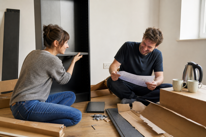 Assembling a bookcase together Couple in their late twenties assembling flat-pack furniture together on a living room floor, laughing over the instruction sheet, boxes and an Allen key nearby