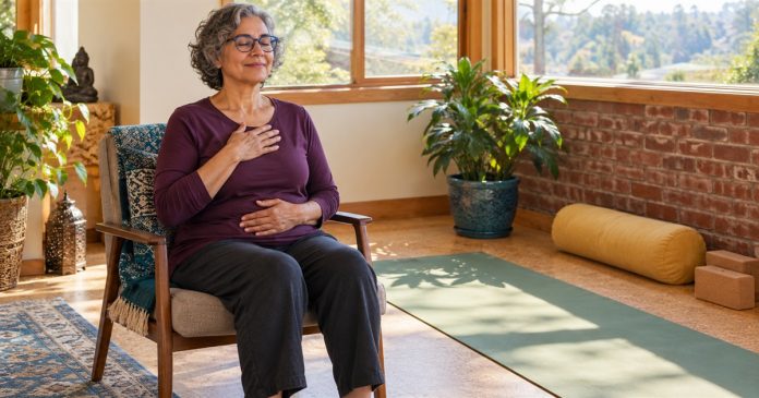 A woman practices a seated rest variation beside a yoga mat.