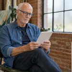 The Guide to Reiki Energy: What the Word Means and What the Evidence Shows An older man in glasses reads an unbranded e-reader in a bright brick-walled studio.