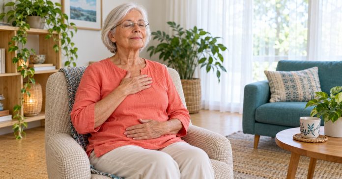 An older woman rests her own hands on her chest and abdomen during seated Reiki self-practice.