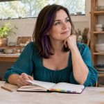 Chakra Out of Balance: What the Phrase Means, in Brief A woman reflects beside an open journal with colored tabs in a pottery studio.