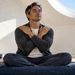 Using Reiki: The Three Ways, in Brief A man rests his own hands on his shoulders during seated Reiki self-practice.