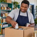 What Is a Lightworker? Six Reflection Prompts and Practical Ways to Help A man sorts sealed food tins into a donation box at a community pantry.