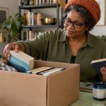 Non-Attachment: What It Really Means, Why It Isn’t Detachment, and Practices for Things, People and Thoughts A woman sorts books into a donation box in a bright room.