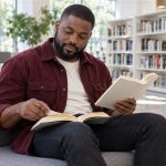 Reiki as “Alternative Healing”: Why Complementary Is the Honest Word A man compares two paperback books while sitting in a bright library reading nook.