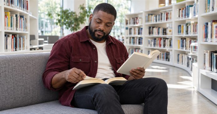 Reiki as "Alternative Healing": Why Complementary Is the Honest Word — editorial cover A man compares two paperback books while sitting in a bright library reading nook.