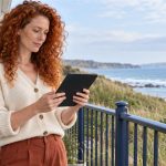 Misunderstandings of Reiki: Where They Come From, in Brief A red-haired woman reads a compact tablet on a quiet coastal balcony.