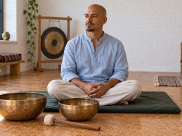 Sound Baths: What Research Suggests, What It Doesn’t, and How to Attend Safely A man sits beside two bronze singing bowls in a community music room.